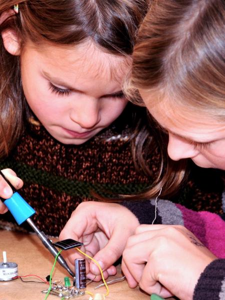 Zwei Kinder löten elektronische Komponenten zu einem kleinen Instrumend zusammen.