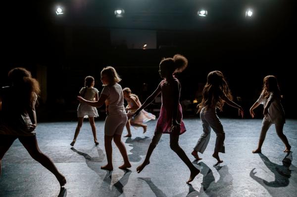 Ferienworkshop mit Tanja Kontny im Ringlokschuppen Ruhr Kinder, die auf einer Bühne Tanzen. Das Licht kommt von schräg oben, wodurch ein Schattenspiel entsteht, dass eher die Silhouetten und weniger Details erkennen lässt.
