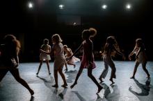 Kinder, die auf einer Bühne Tanzen. Das Licht kommt von schräg oben, wodurch ein Schattenspiel entsteht, dass eher die Silhouetten und weniger Details erkennen lässt.